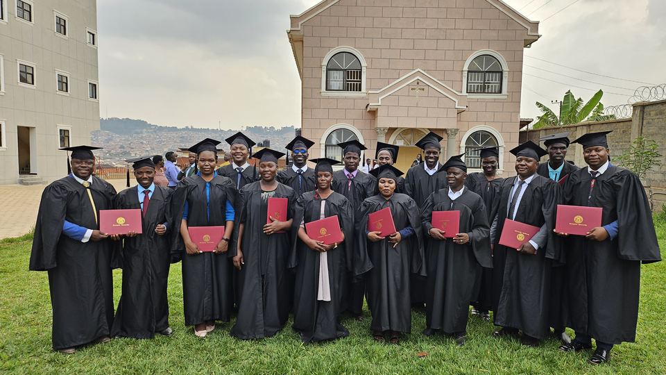 Graduates in black gowns and caps holding red diploma folders on a lawn