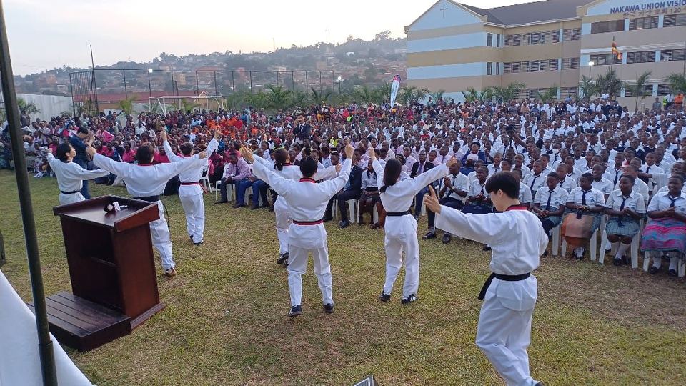 Performers in white uniforms in front of students seated on the school field